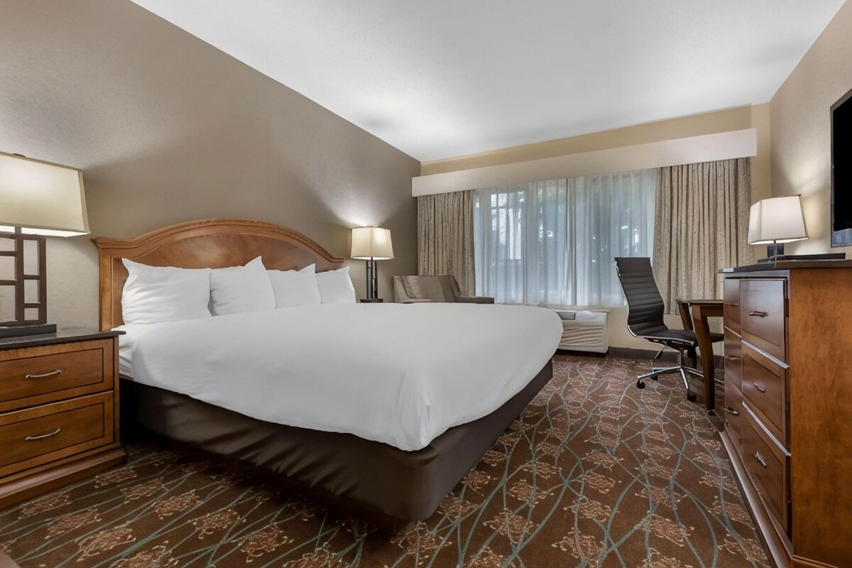 Une chambre d’hôtel avec un grand lit, un bureau, une chaise, une commode et un téléviseur.