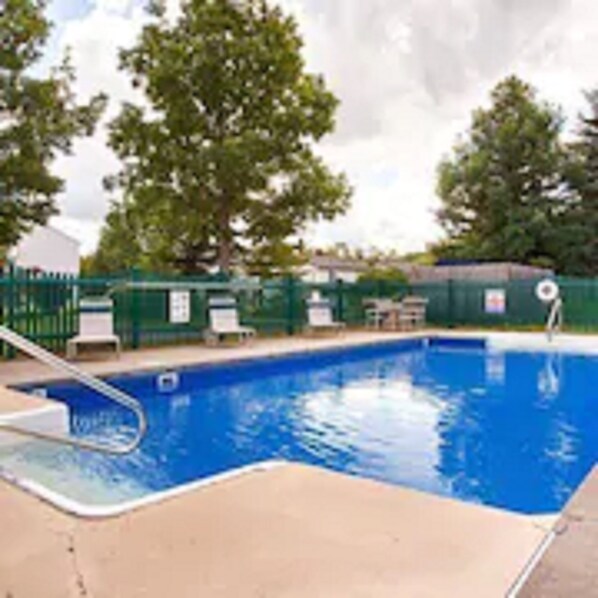 A rectangular swimming pool with a ladder on one side, surrounded by a green fence and trees.
