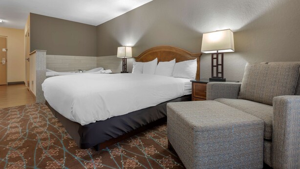 A hotel room with a large bed, two bedside lamps, a grey armchair, and a patterned rug.