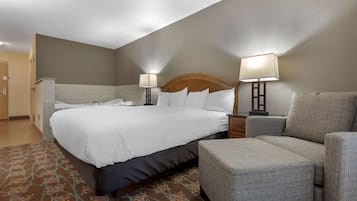 A hotel room with a large bed, two bedside lamps, a grey armchair, and a patterned rug.