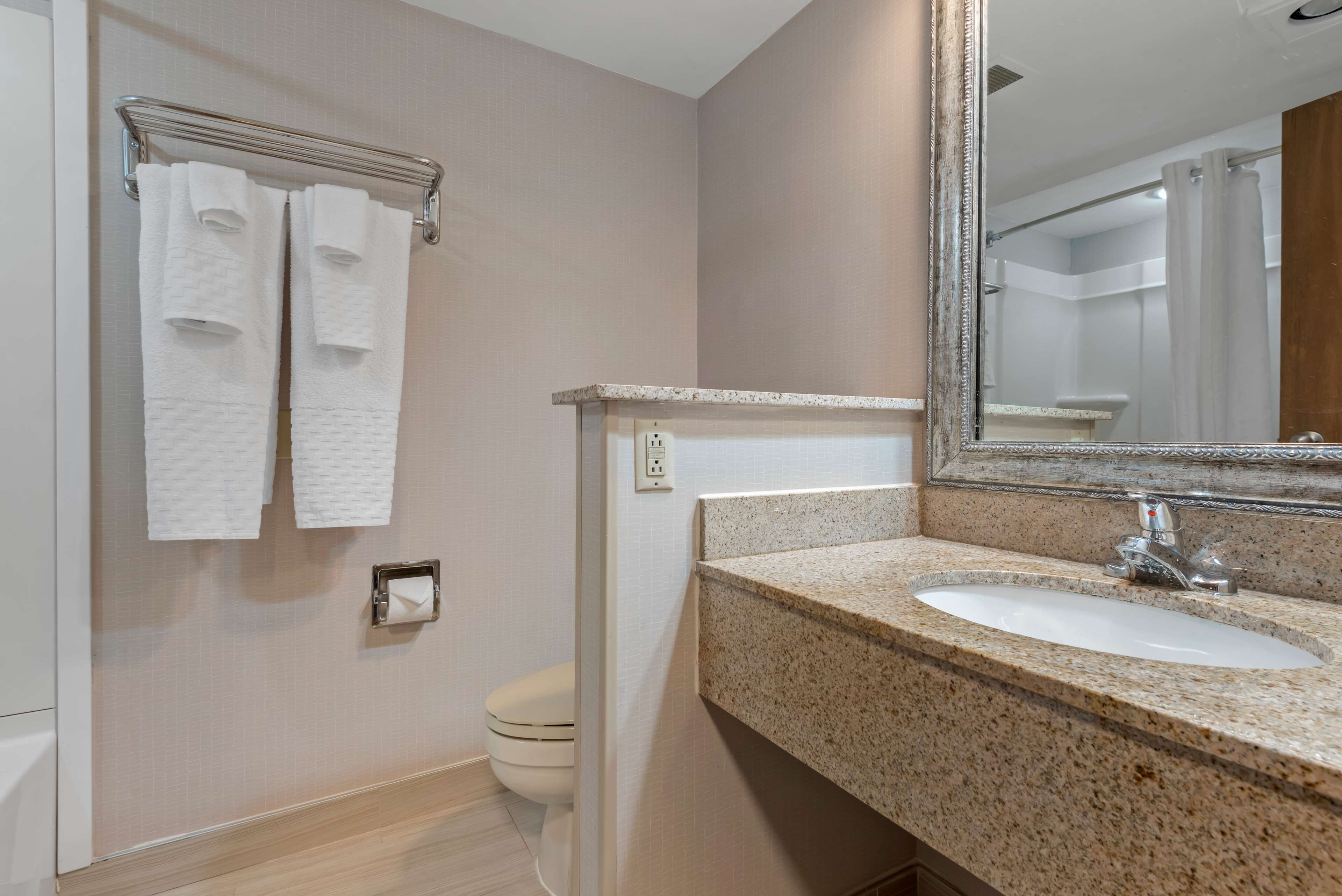 Une salle de bain avec un lavabo doté d’un plan de travail en granit, un miroir et deux serviettes blanches suspendues à un porte-serviettes en métal.