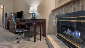A hotel room with a desk, chair, TV, lamp, and a fireplace. - Best Western University Inn (Ithaca)