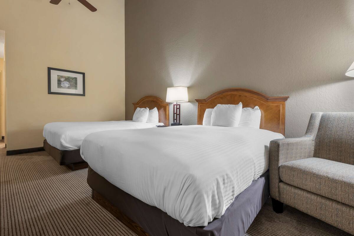 A hotel room with two beds, a chair, a lamp, and a framed picture on the wall.