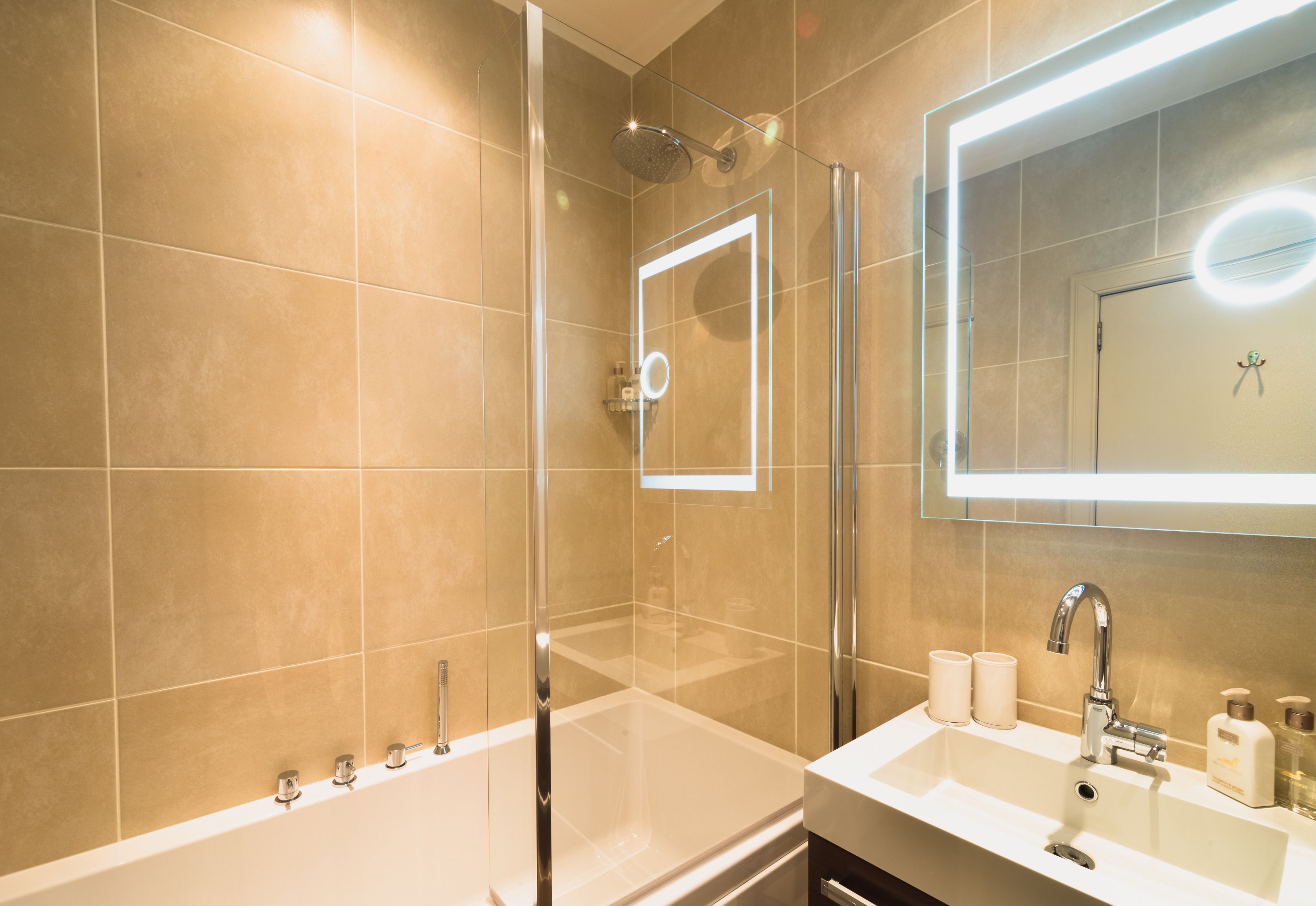 Une salle de bain moderne avec une douche à parois de verre, un grand miroir et un meuble-lavabo avec un évier et des articles de toilette.