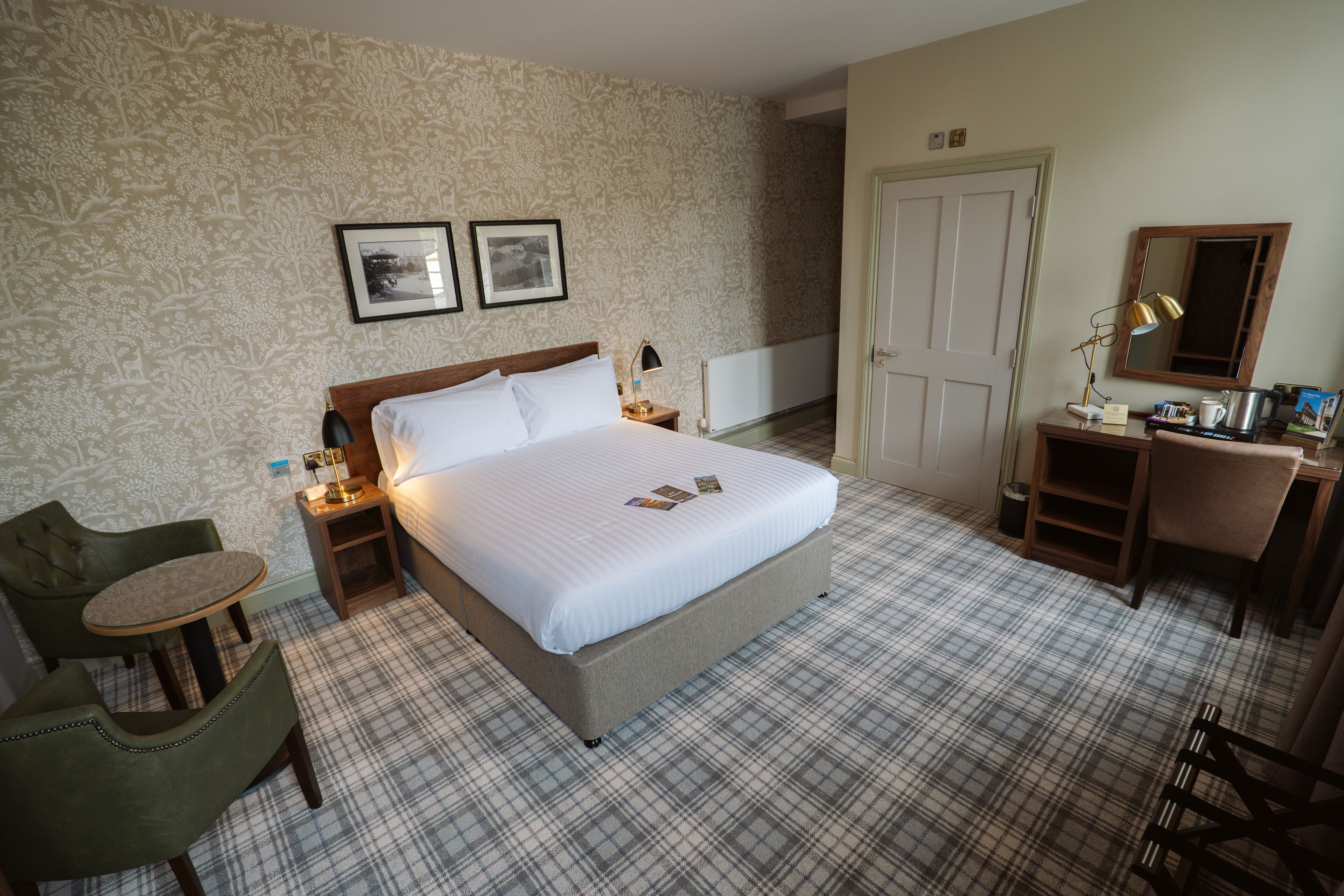 Een hotelkamer met een groot bed, twee nachtkastjes, een bureau met stoel, een klein rond tafeltje en een stoel.