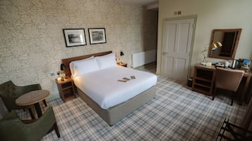 Een hotelkamer met een groot bed, twee nachtkastjes, een bureau met stoel, een klein rond tafeltje en een stoel.