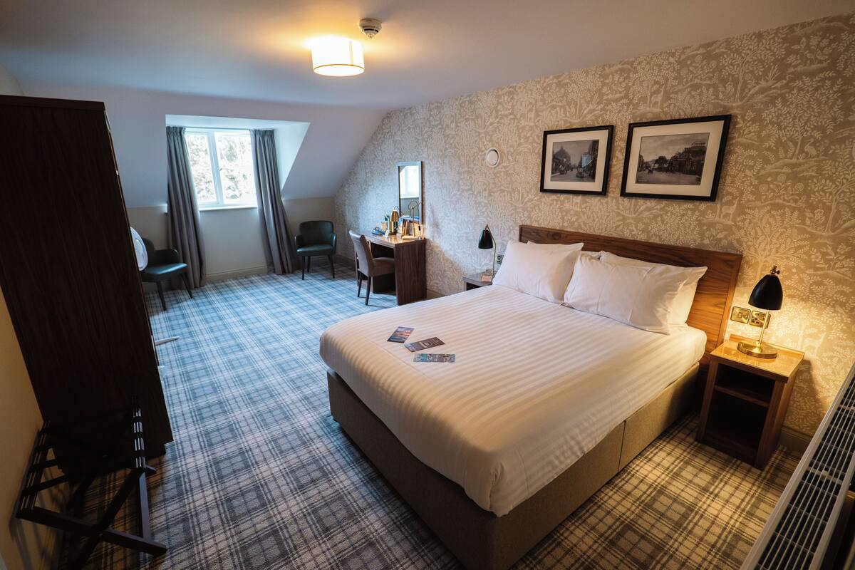 A hotel room with a large bed, a desk, a chair, and a window.