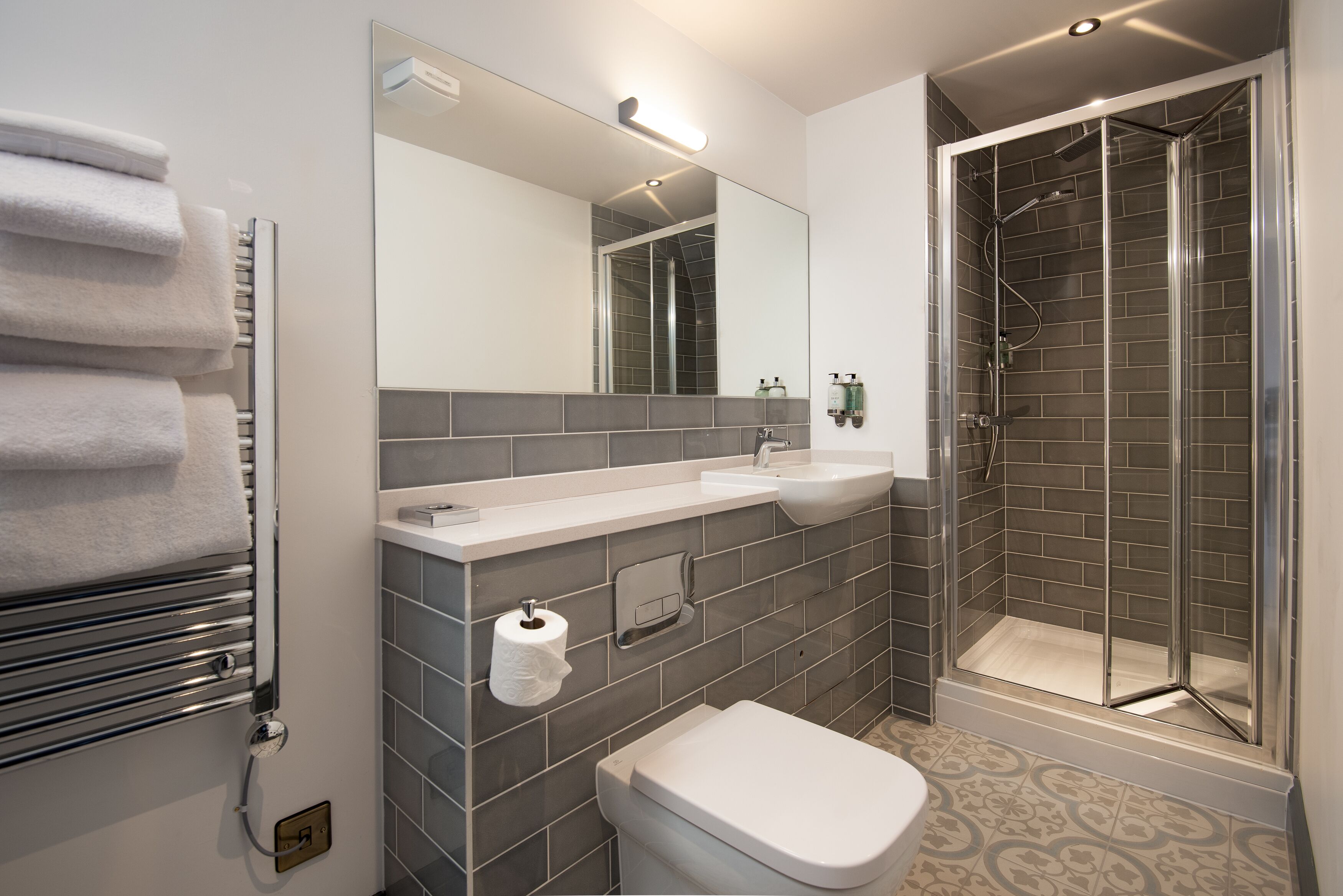 Een moderne badkamer met een douchecabine van glas, een witte wastafel en een handdoekhouder.