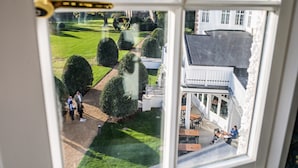 A view from a window overlooking a well-maintained lawn with neatly trimmed bushes, a pathway, and a building with a white facade and a dark roof. - The Ripon Inn - The Inn Collection Group (Ripon)