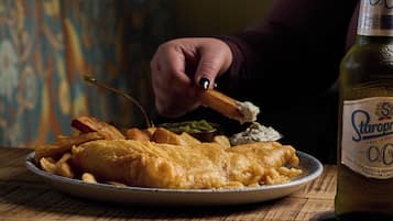 A plate of fish and chips with a bottle of beer on the side.