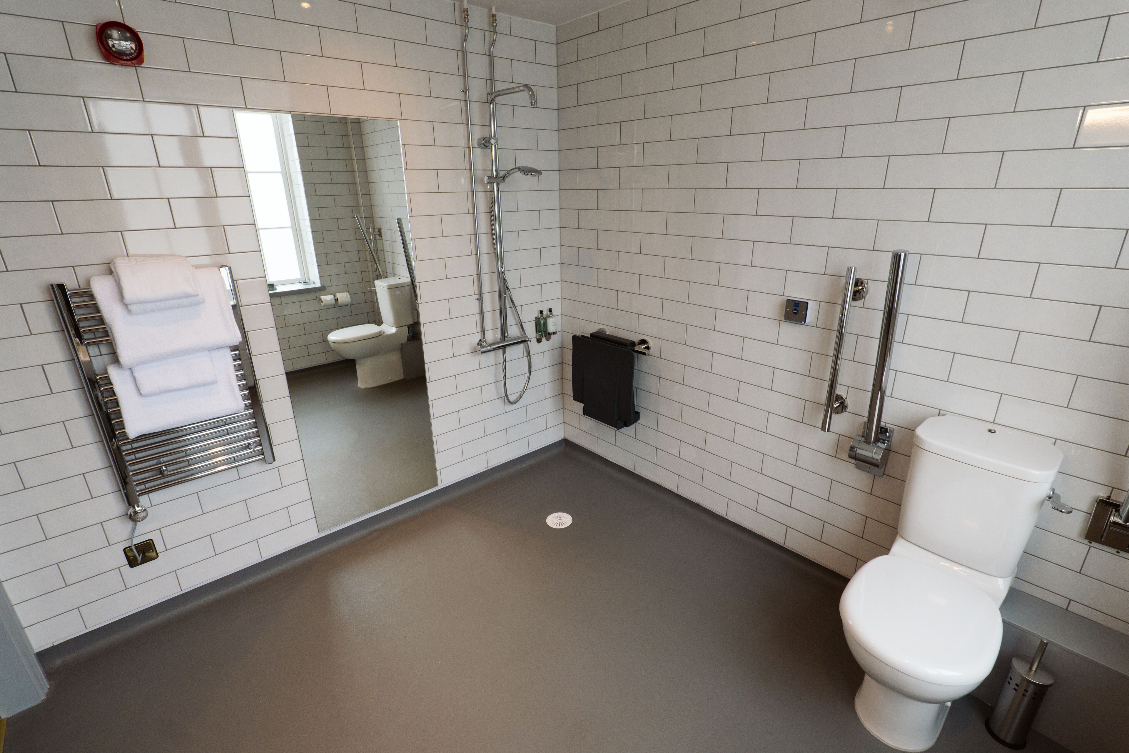 A modern bathroom with white tiled walls, a white toilet, a shower with a glass enclosure, and a towel rack with folded towels.