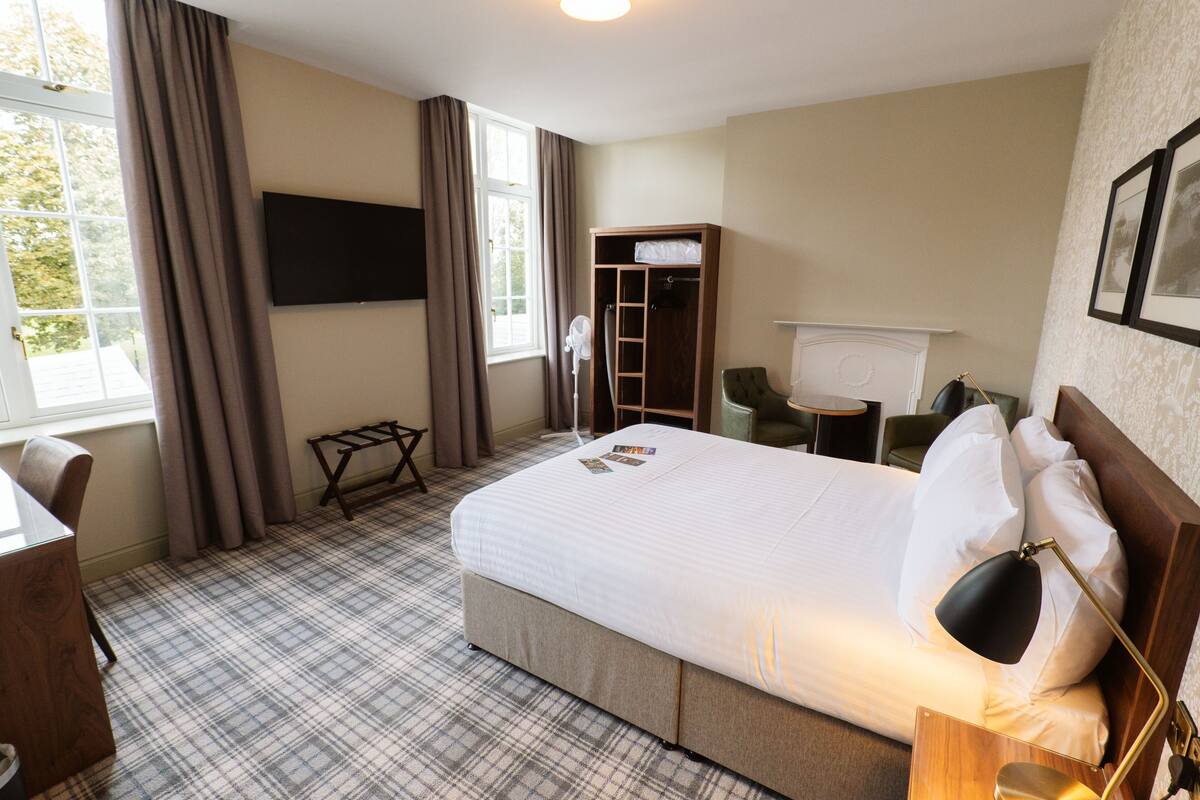 A hotel room with a bed, a desk, a chair, a TV, and a window with curtains.