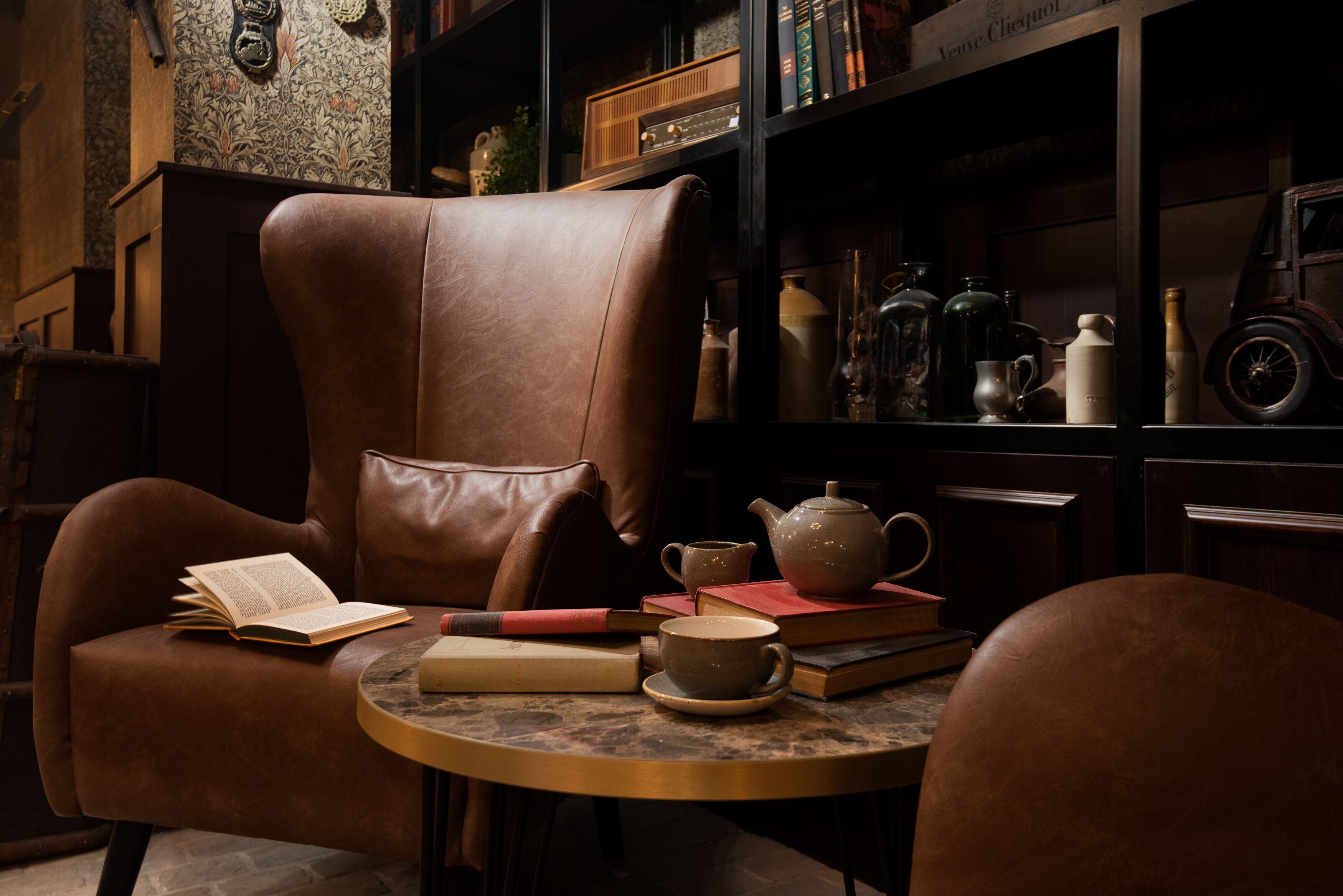 Un sillón de cuero con un libro abierto y una tetera sobre una mesa redonda.