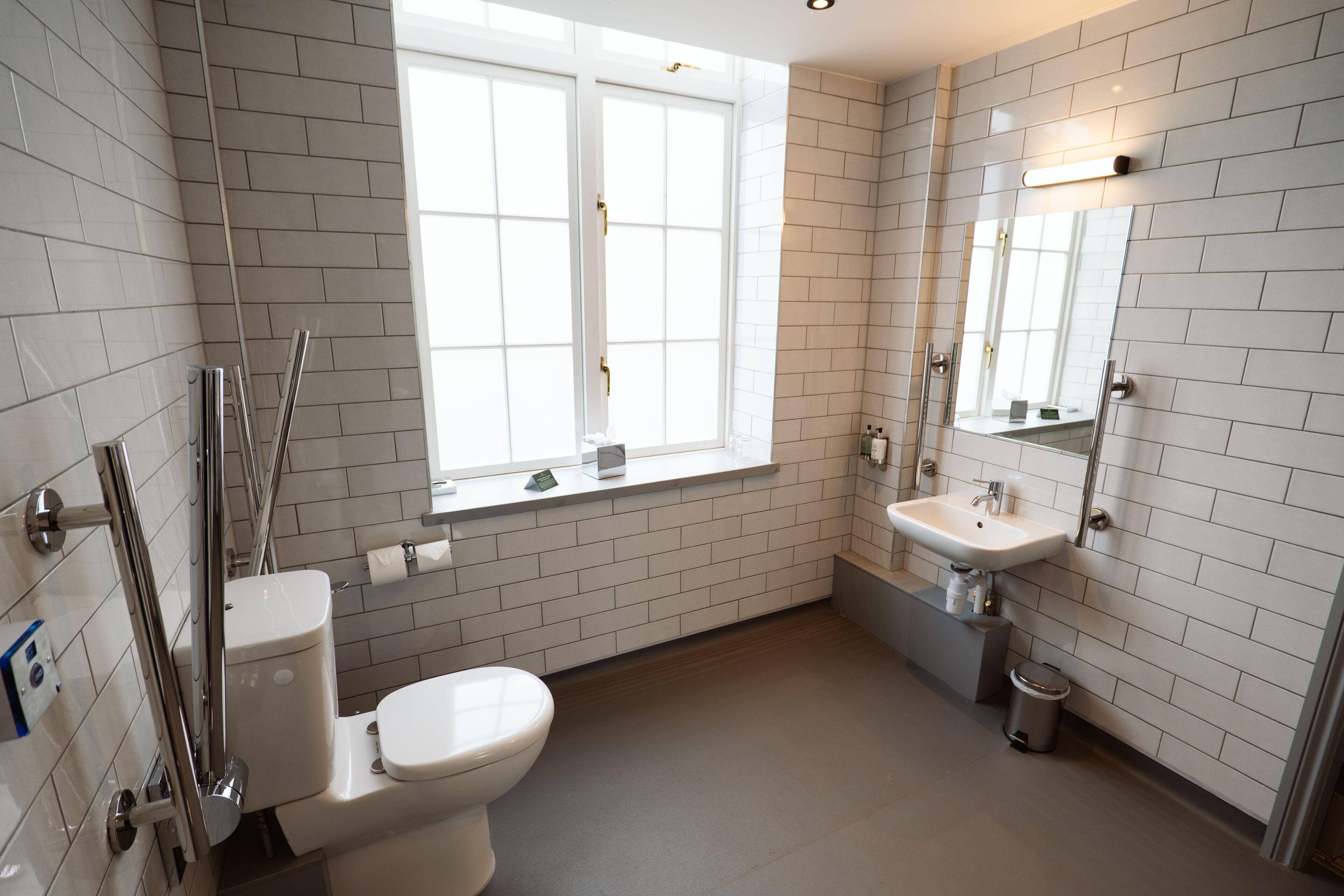 A modern bathroom with white subway tiles, a toilet, a sink, and a window.