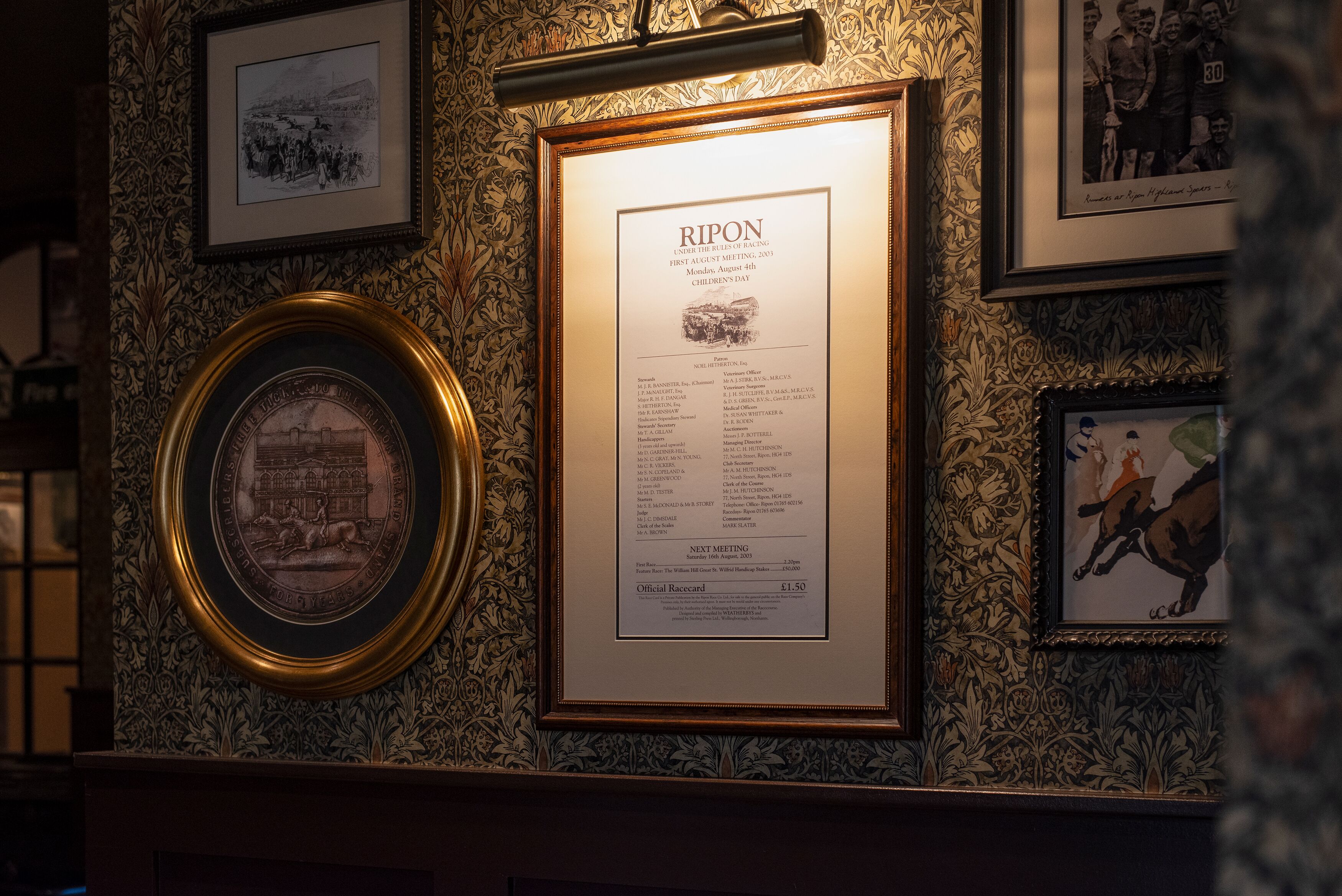 A framed document titled "RIPON" with a list of names and details, set against a wall with ornate wallpaper.