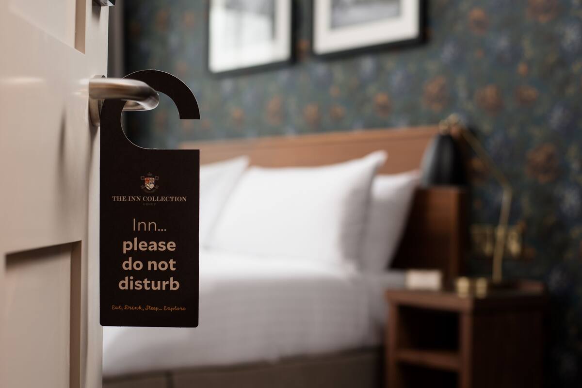 A hotel room with a bed, a nightstand, and a sign on the door that reads "The Inn Collection please do not disturb."