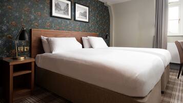 A double bed with a wooden headboard, a nightstand with a lamp, and a plaid-patterned rug.