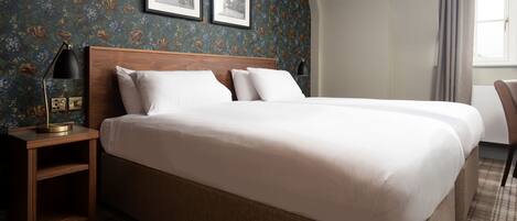 Una cama doble con cabecera de madera, una mesita de noche con lámpara y una alfombra estampada de pata de gallo.