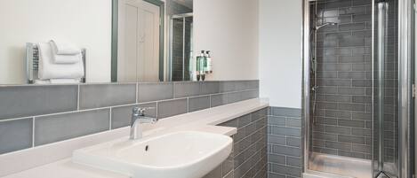 A modern bathroom with a white sink, grey tiles, a glass shower enclosure, and a mirror with a towel rack.