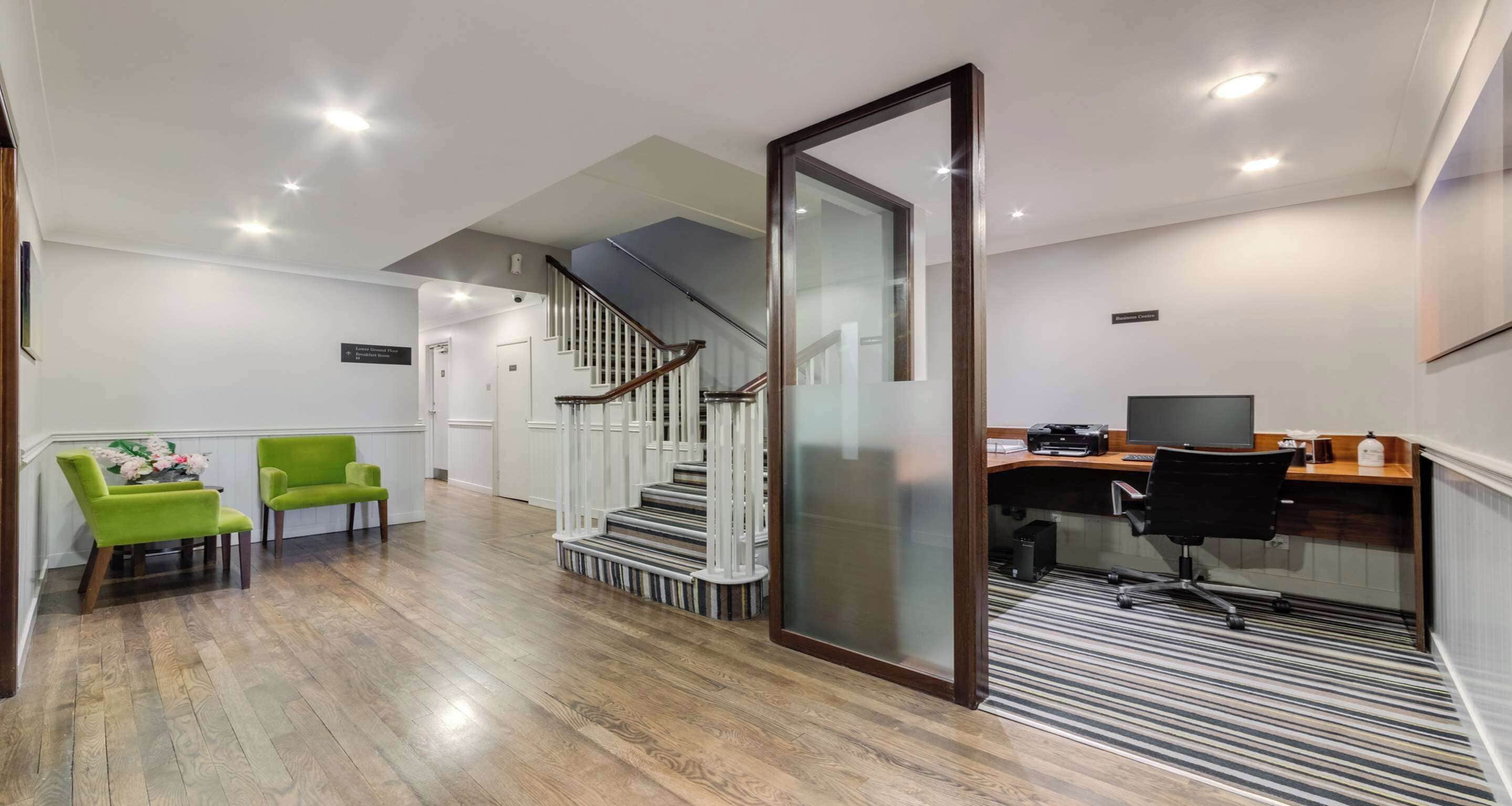 A modern office space with a wooden floor, a staircase, a desk with a computer, and two green chairs.