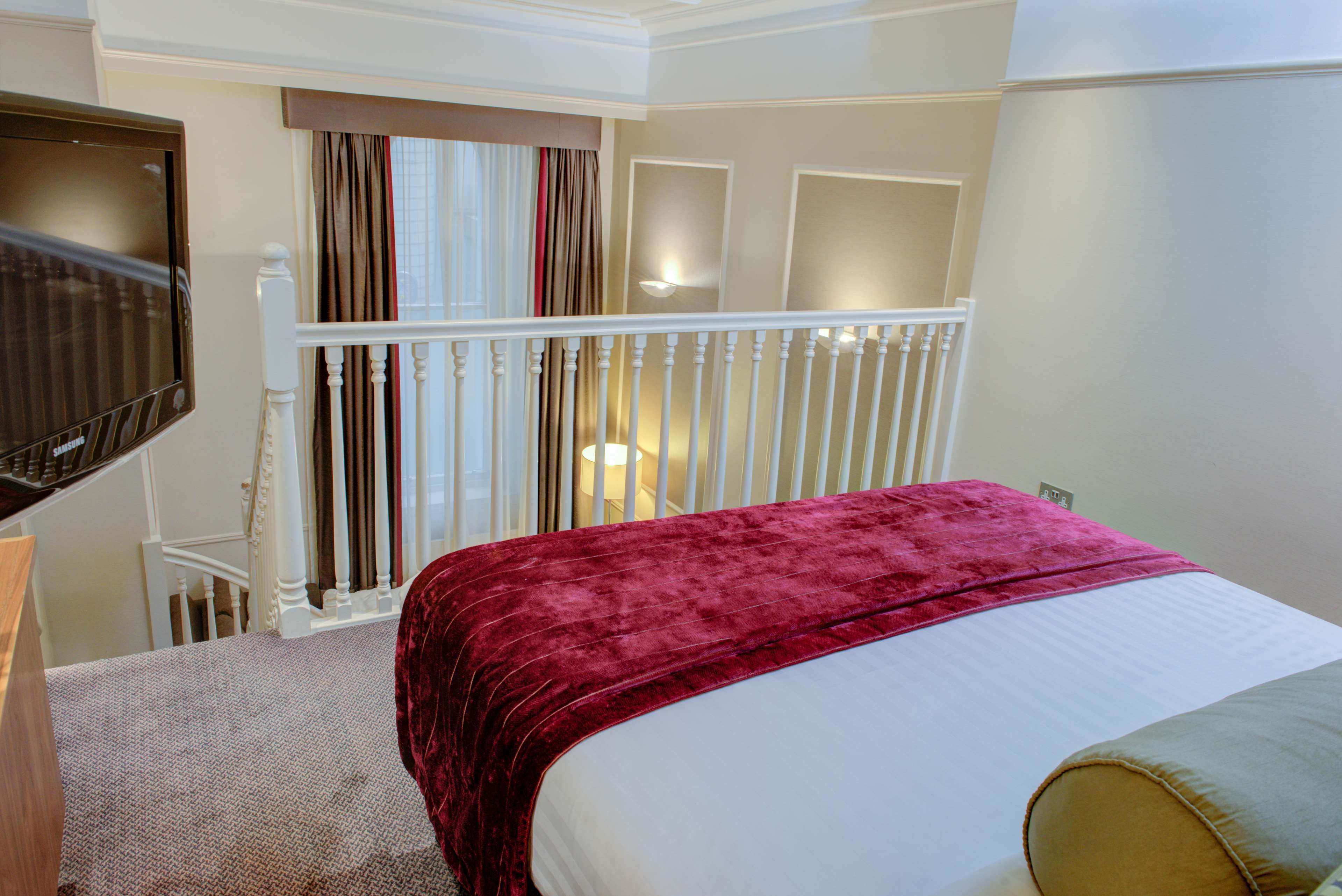 Una habitación de hotel con una cama, un televisor, una escalera y una ventana con cortinas.