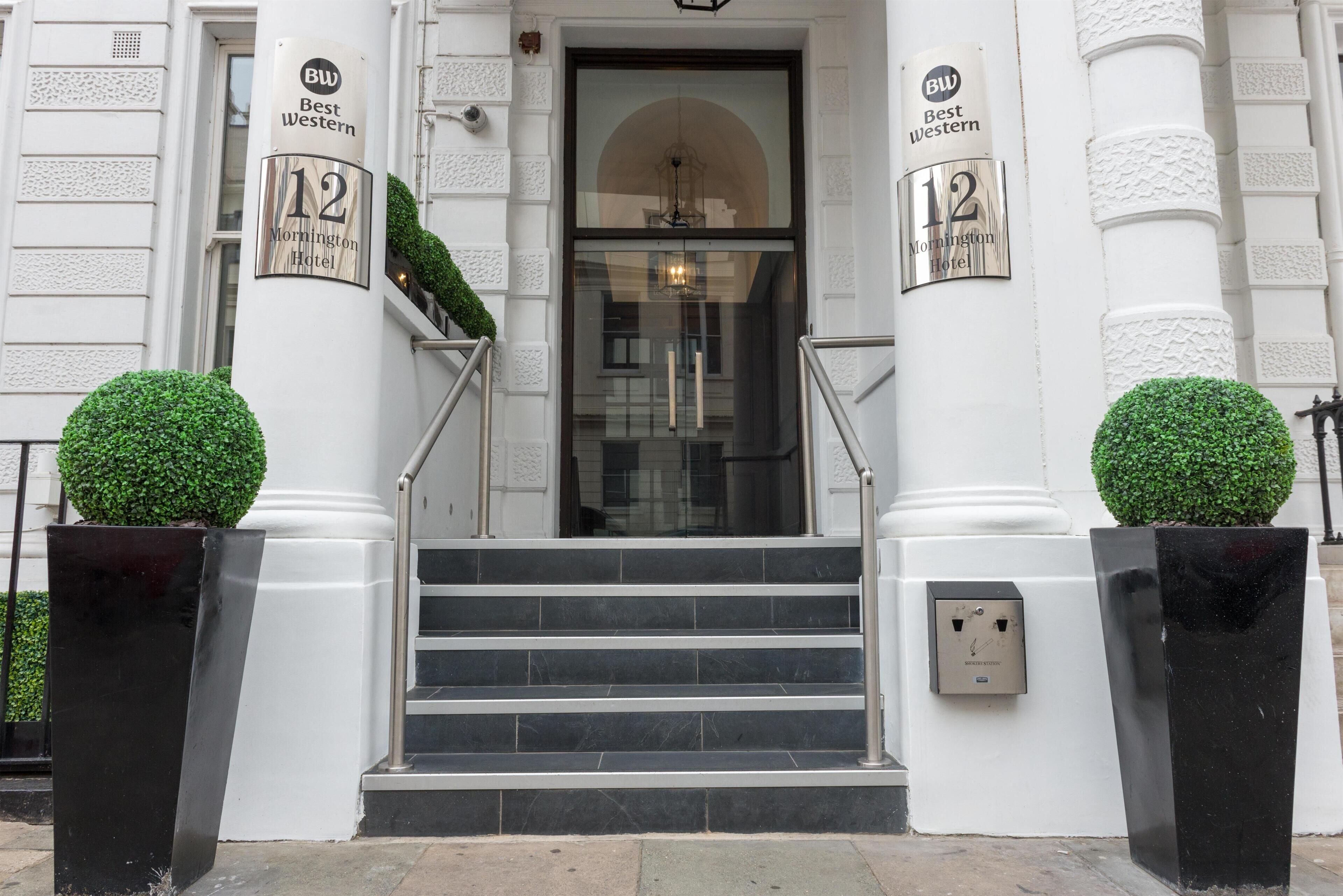 A hotel entrance with a double door, two columns with signage, a staircase, and a small potted plant on each side.