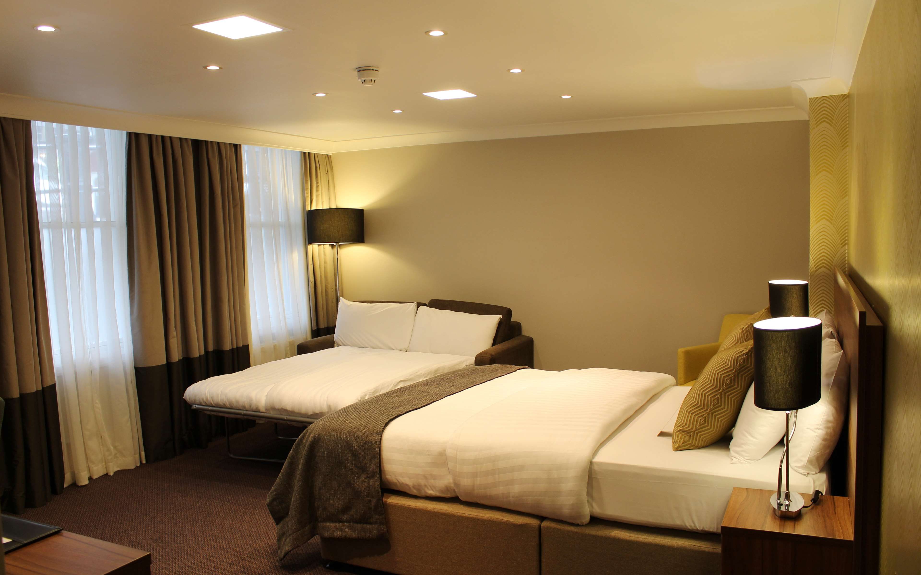 A hotel room with two beds, a desk, a lamp, and a window with curtains.