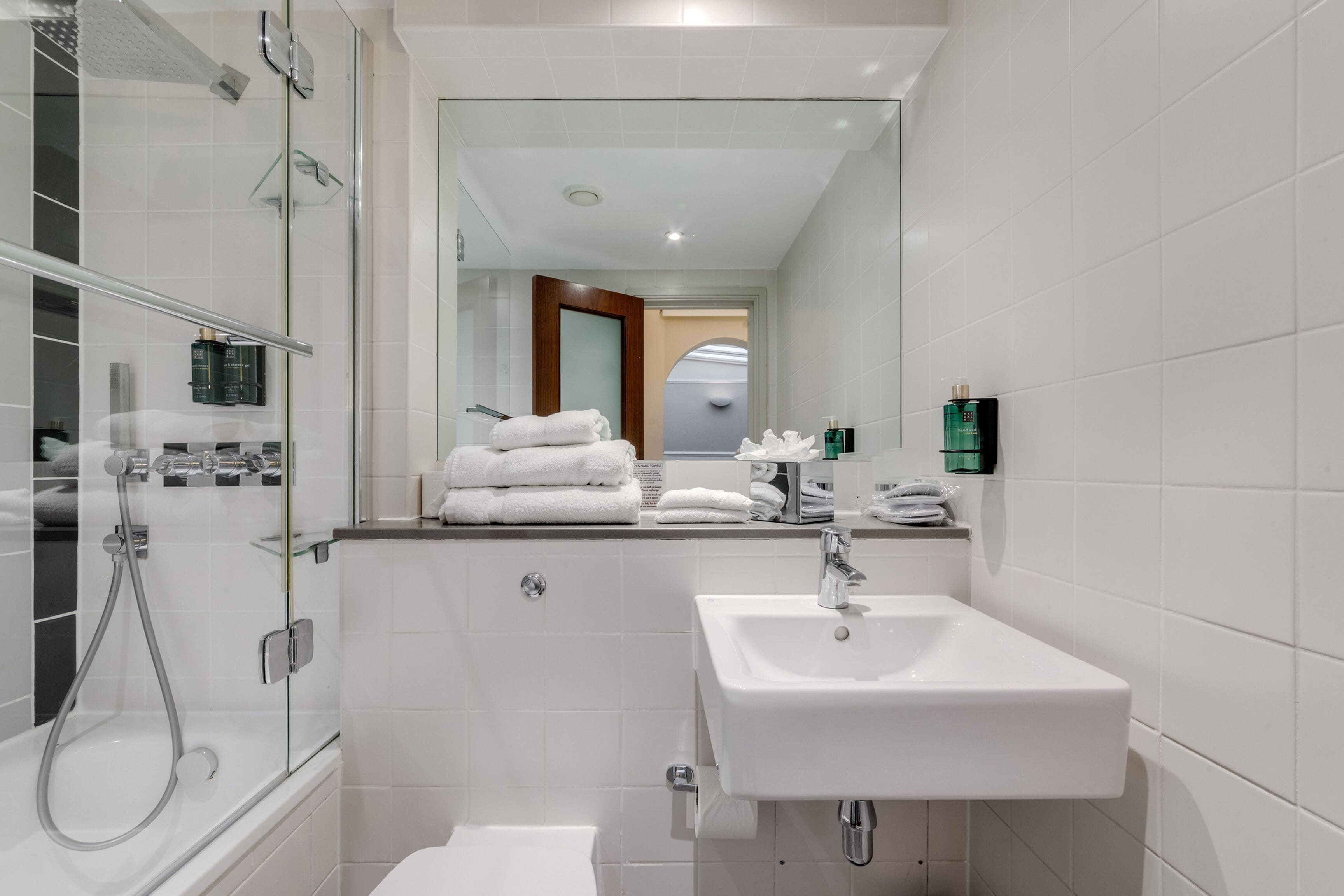 Une salle de bain moderne avec une douche à parois de verre, un lavabo blanc et des serviettes soigneusement pliées.