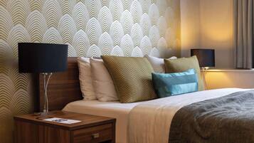 A hotel room with a bed, nightstand, lamp, and patterned wallpaper.