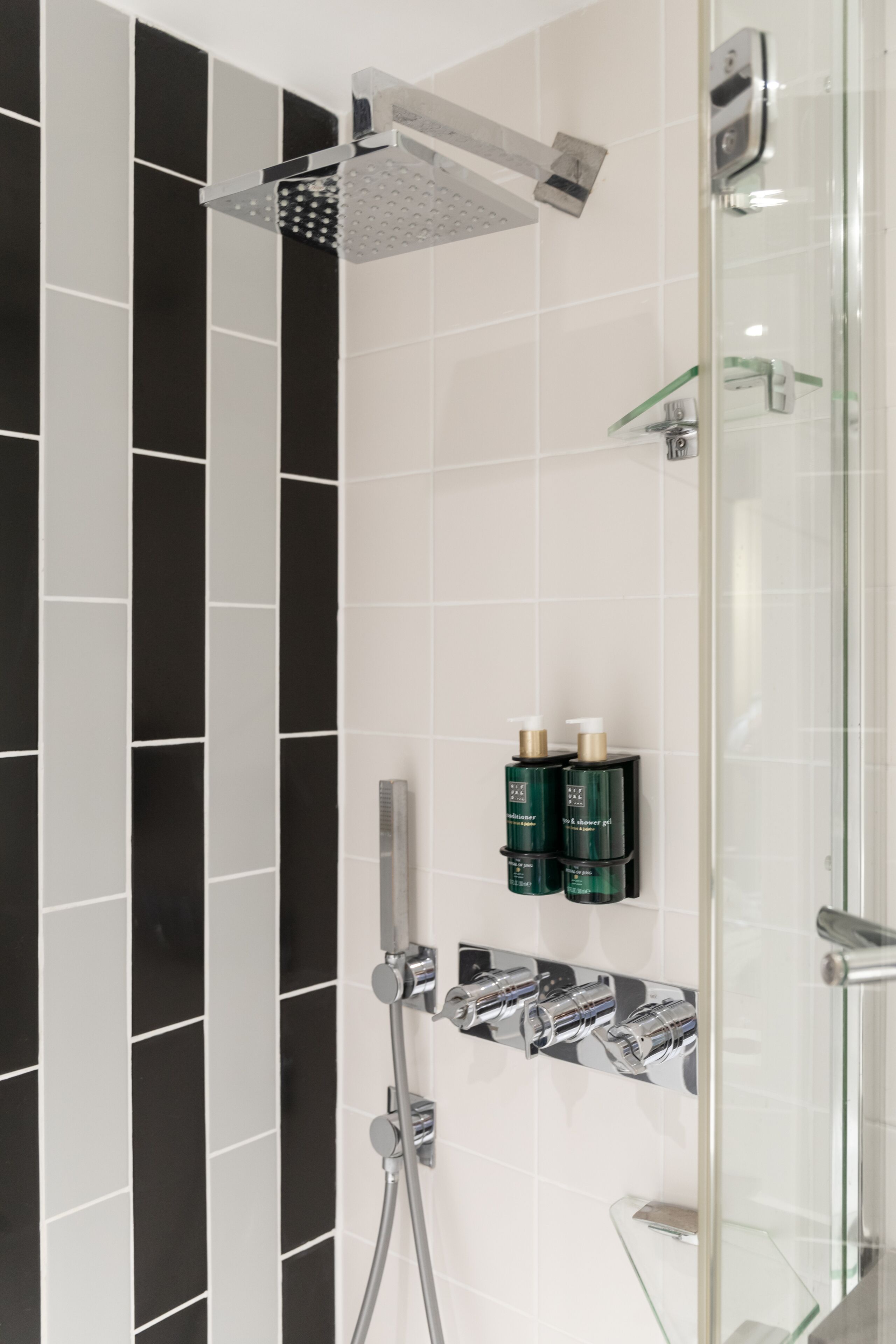 A modern bathroom with a glass shower enclosure, chrome fixtures, and black and white tiles.