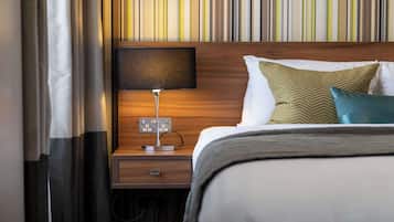 Una cama bien hecha con almohadas y una mesita de noche con lámpara.