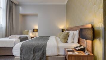A hotel room with two beds, a wooden nightstand with a phone and remote, and a wall with a patterned wallpaper.