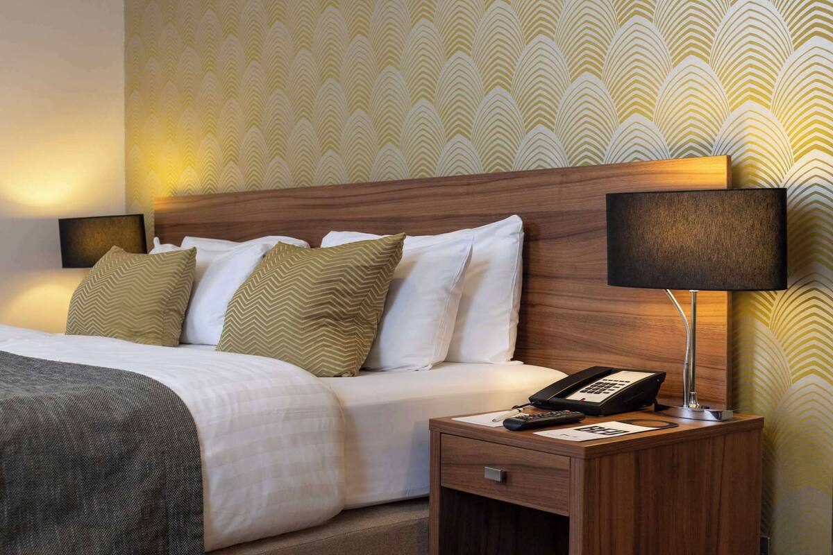 A hotel room with a bed, bedside lamps, a telephone, and a nightstand.