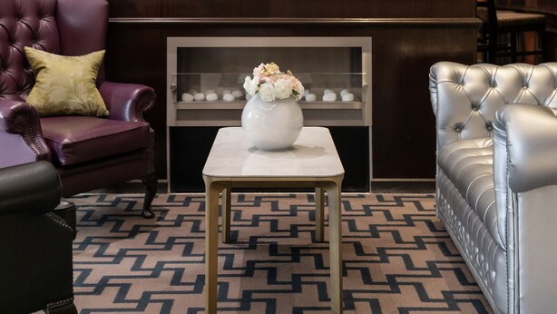 A room with a fireplace, framed black and white photographs, a marble fireplace surround, a patterned carpet, and leather furniture. - Best Western Mornington Hotel London Hyde Park (London)