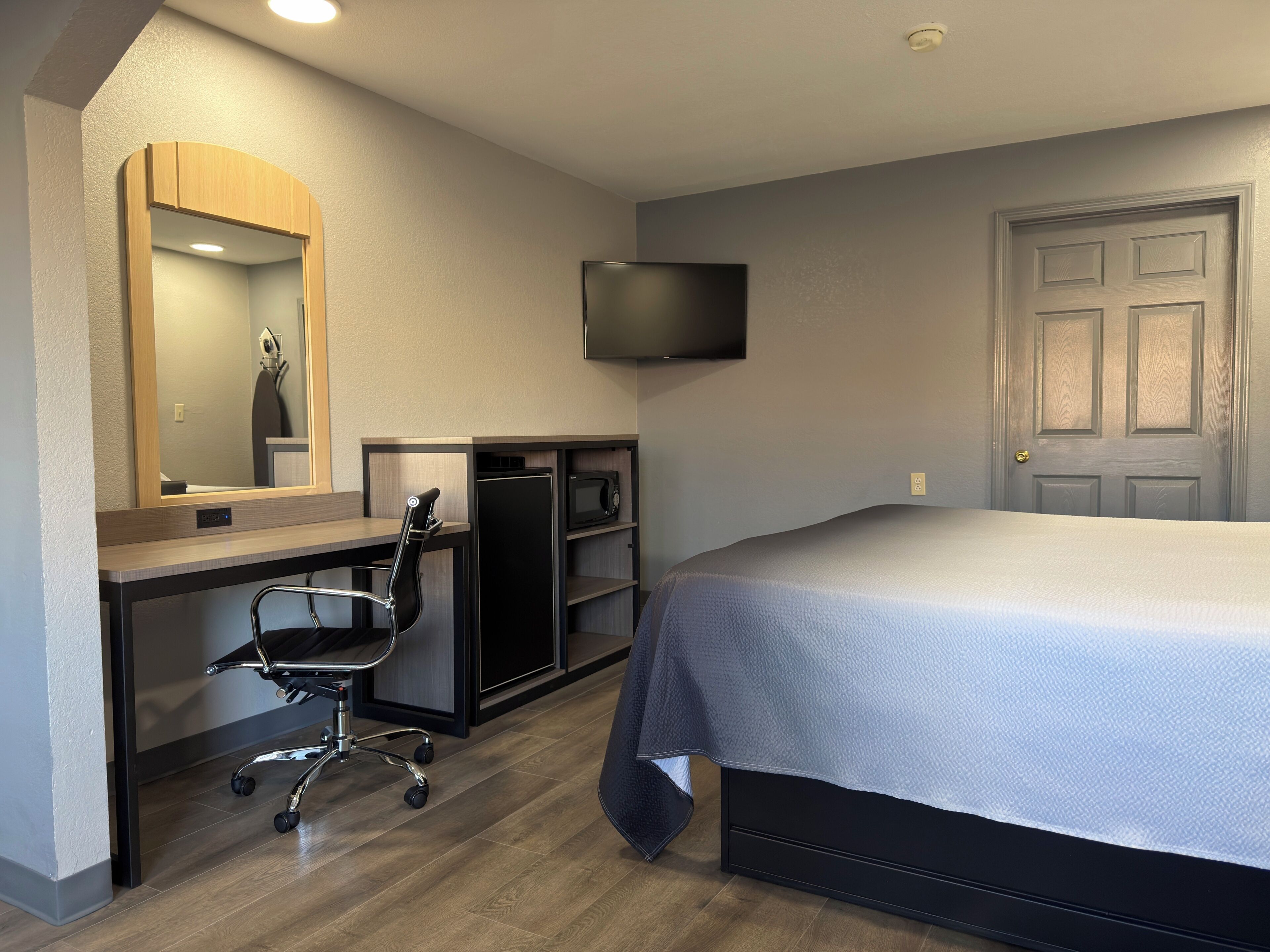 Une chambre à coucher avec un lit, un bureau et une chaise, une télévision et une porte.