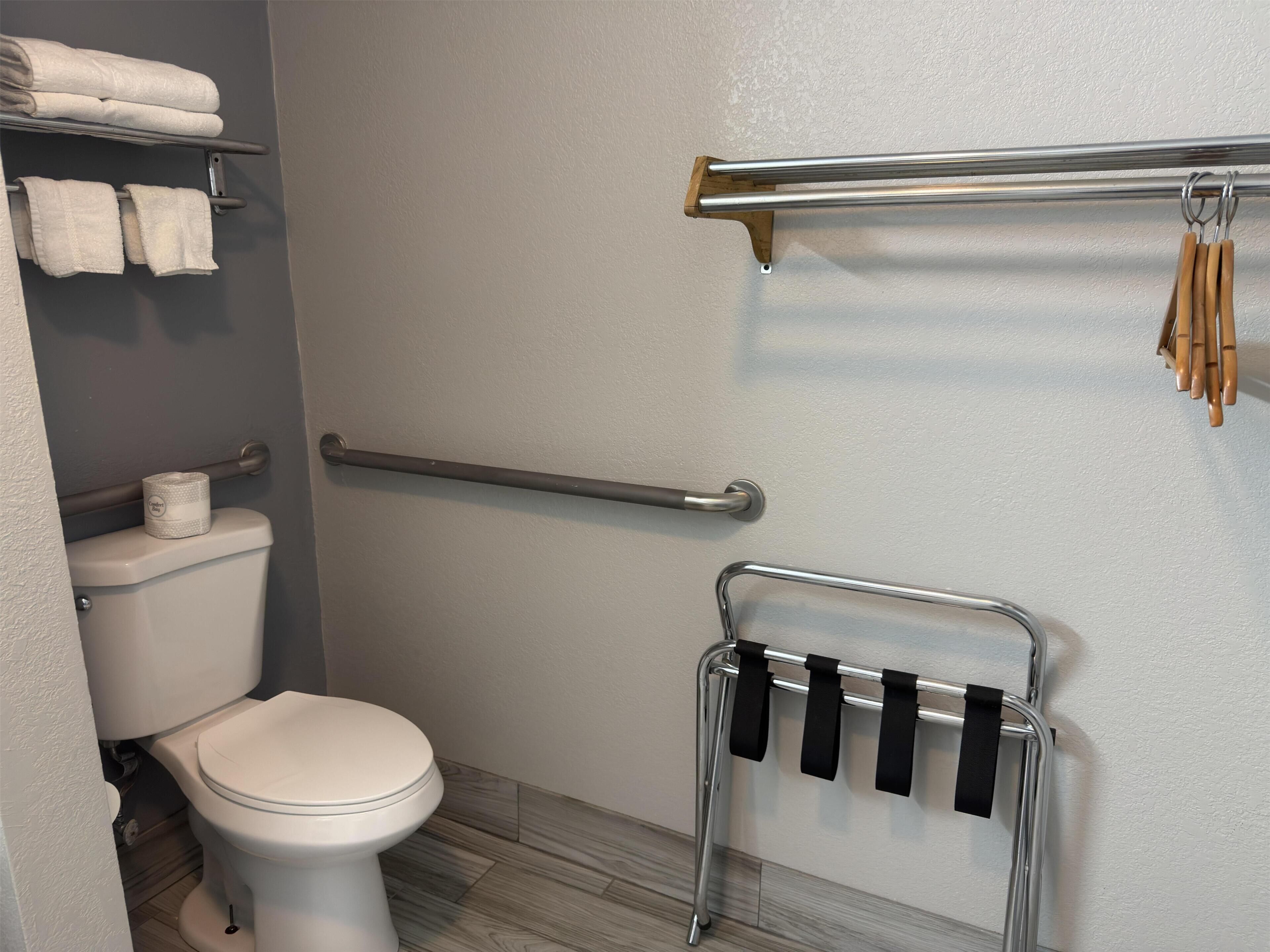 A bathroom with a toilet, a towel rack, a handrail, and a towel dispenser.