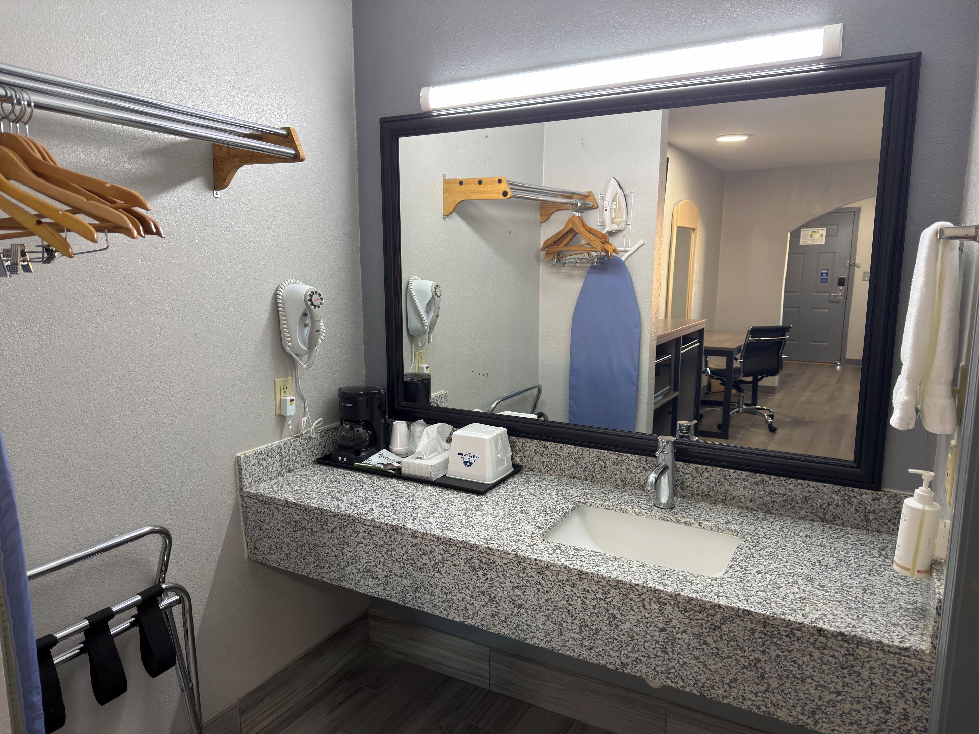 Une salle de bain dotée d’un comptoir en granit, d’un lavabo, d’un miroir, d’un sèche-cheveux, d’un porte-serviettes et d’une machine à café.