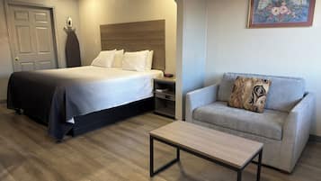 A hotel room with a bed, a sofa, a coffee table, a nightstand, and a wall-mounted fan.