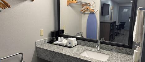 A hotel bathroom with a granite countertop, a sink, a mirror, a towel rack, a shower curtain, and a coffee maker.
