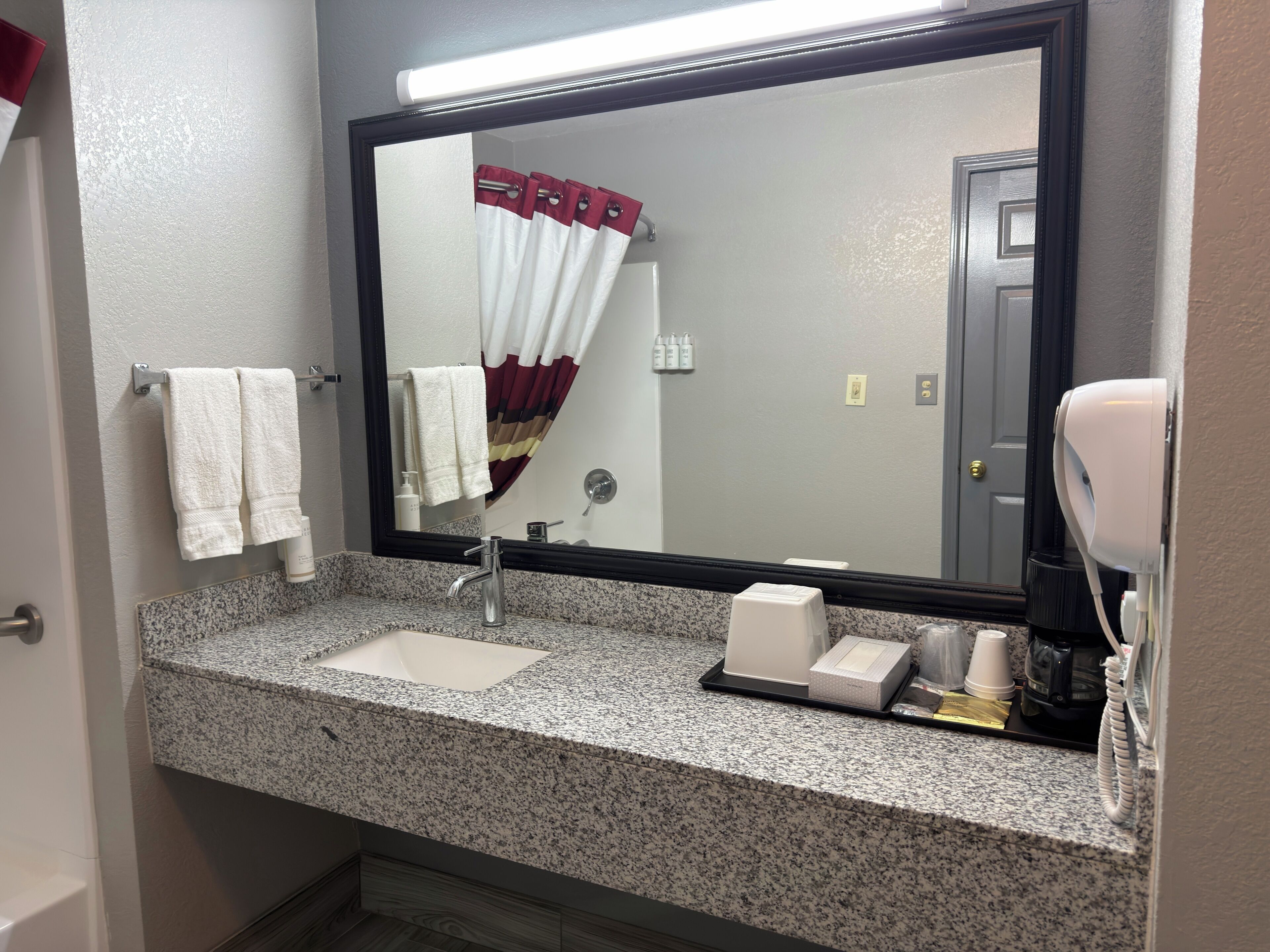 A bathroom with a granite countertop, a sink, a mirror, a towel rack, a shower curtain, and a hairdryer.