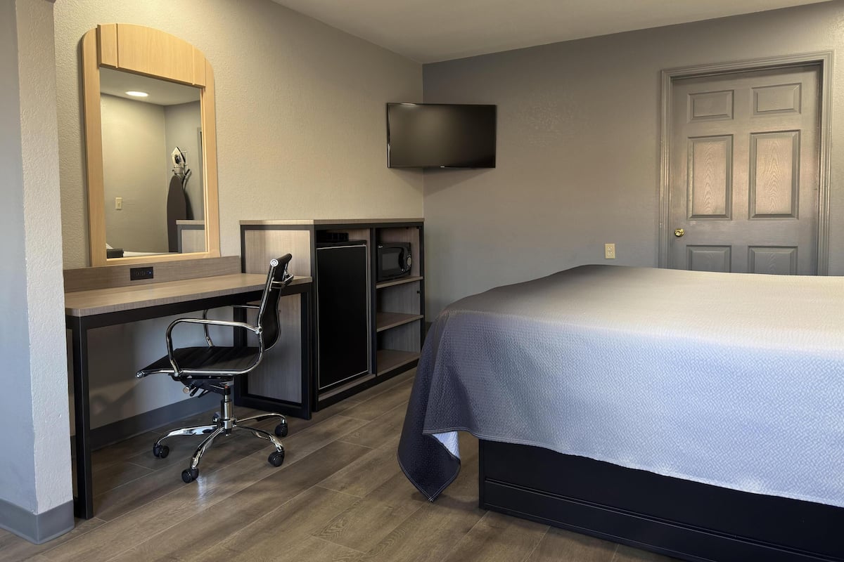 A bedroom with a bed, a desk with a chair, a TV, and a door.