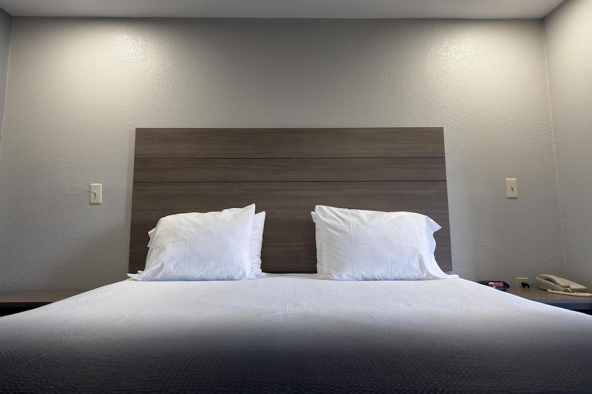 A hotel room with a bed, two bedside tables, a wooden headboard, and a ceiling light.