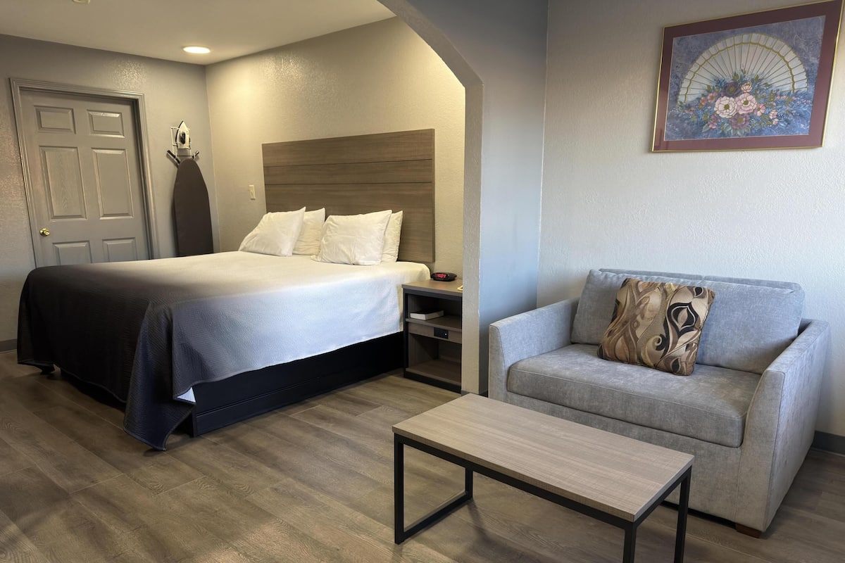 A hotel room with a bed, a sofa, a coffee table, a nightstand, and a wall-mounted clock.