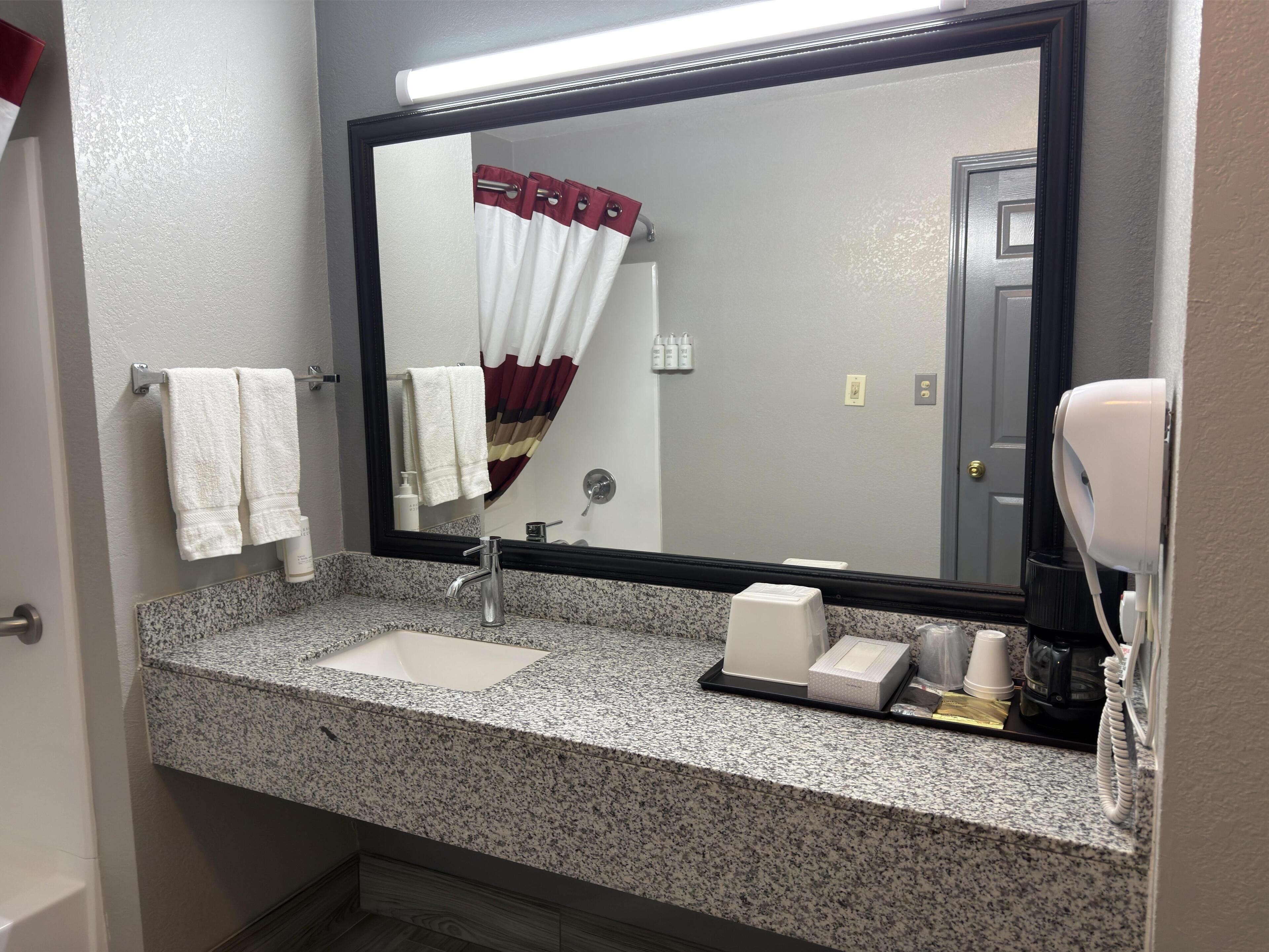 A bathroom with a granite countertop, a sink, a mirror, a towel rack, a shower curtain, and a hairdryer.