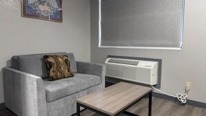 Una sala de estar con un sofá gris, una mesa de centro de madera, un equipo de aire acondicionado y un cuadro en la pared.