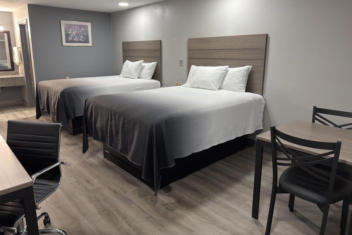 A hotel room with two beds, a desk, and a chair.
