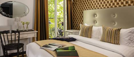 Hotelkamer met een groot bed, een bureau met stoel, een spiegel en een raam met uitzicht op groen.
