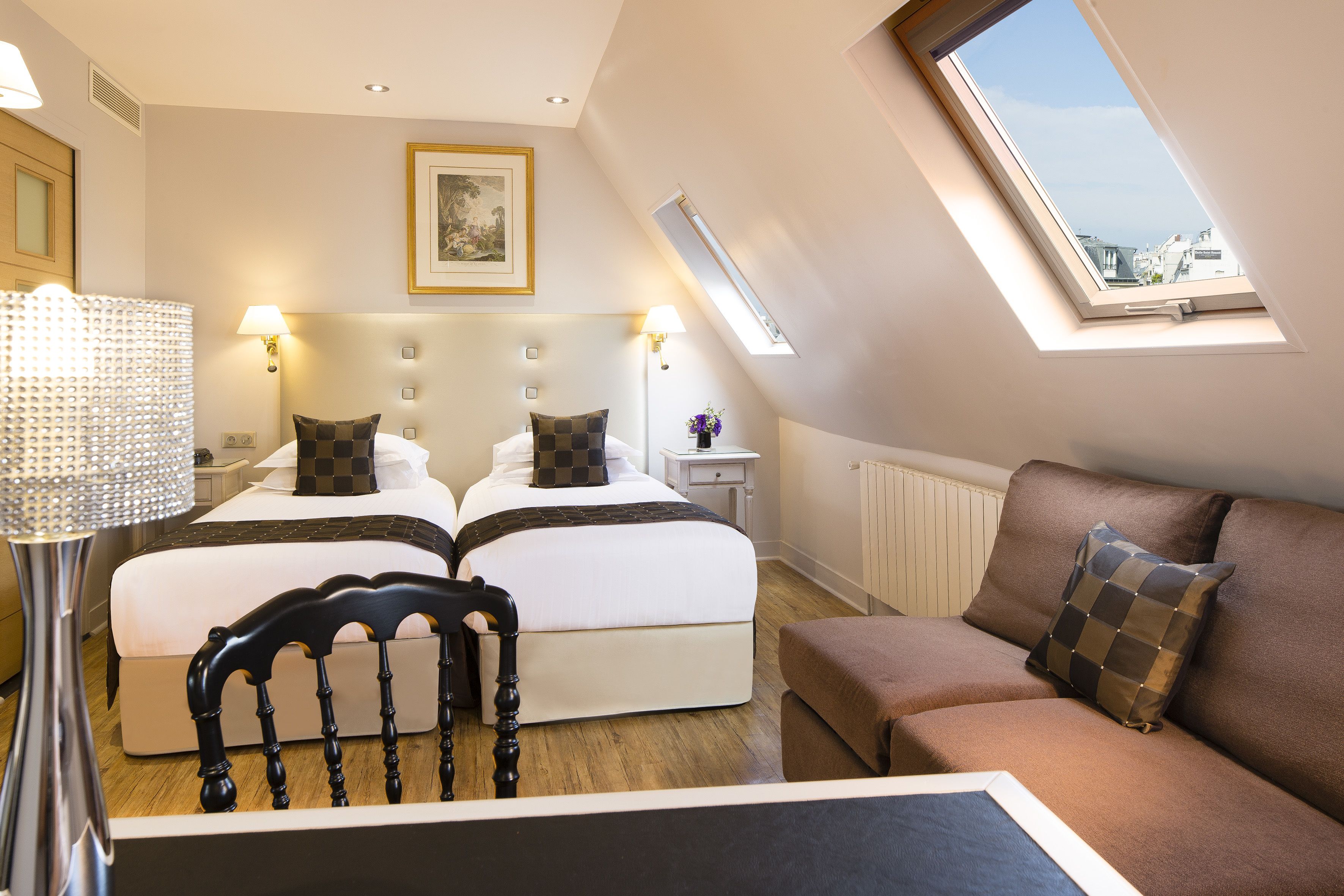 A bedroom with two beds, a sofa, a lamp, and a skylight.