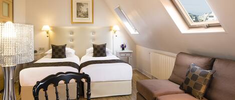 A bedroom with two beds, a sofa, a lamp, and a skylight.
