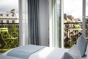 Quarto de hotel com varanda, uma cama com almofadas e vista para a paisagem urbana.